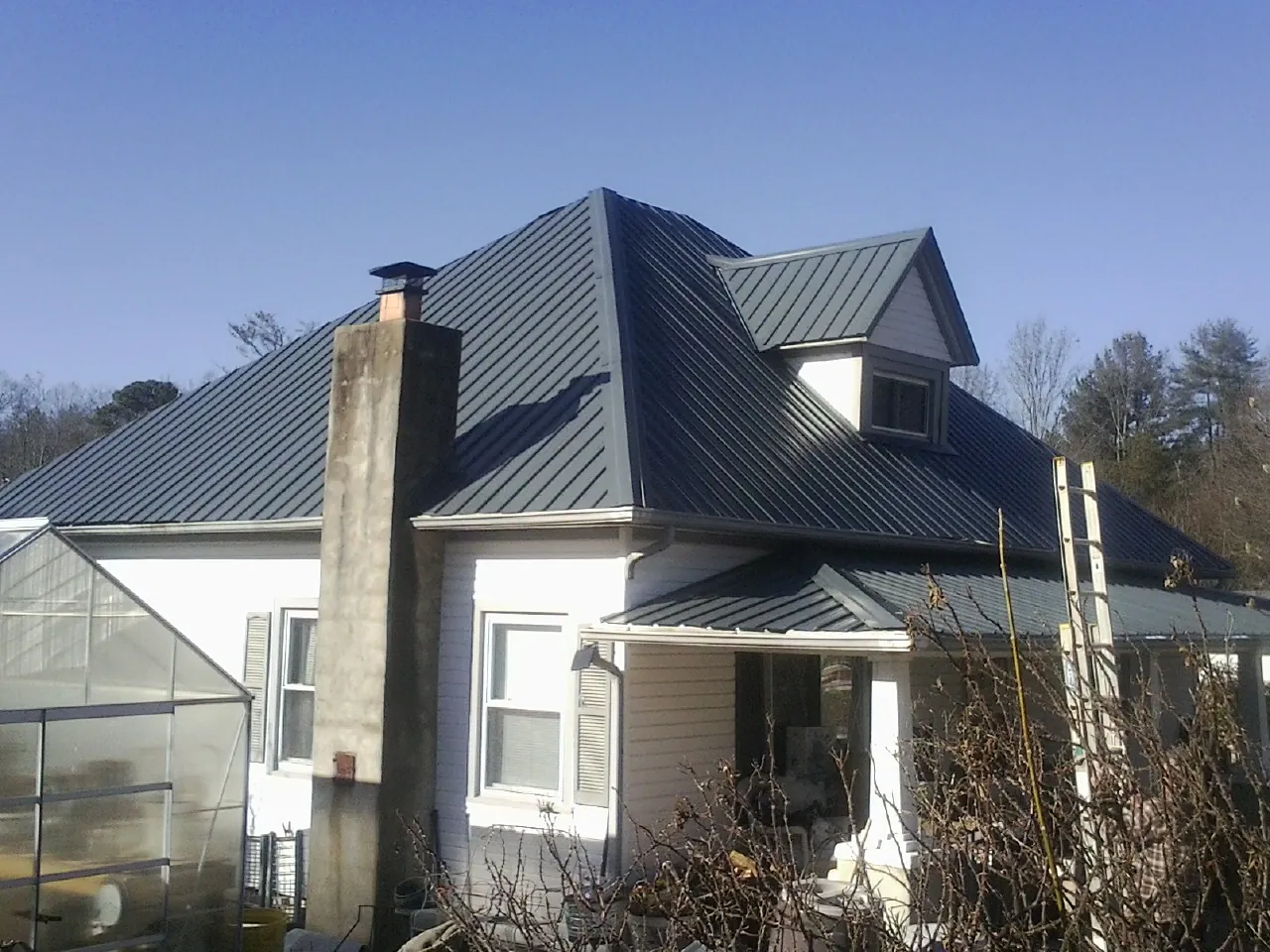 Dark blue standing seam metal roof on a white farmhouse with dormer — Slate & Tile Roof Repair by Roofing Brothers in Shelter Island Heights