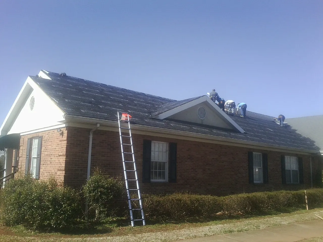 Crew tearing shingles off a brick ranch roof with a ladder set — Emergency Roof Repair work by our crew in Shelter Island Heights