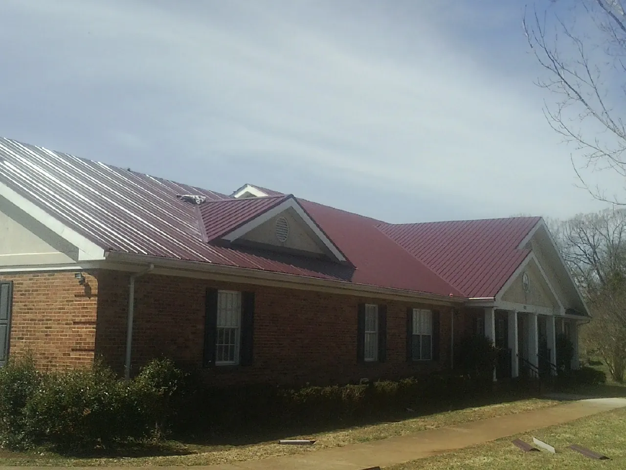 Red metal roof with gabled entries on a long brick building, from a Hail Damage Roof Repair job in Shelter Island Heights