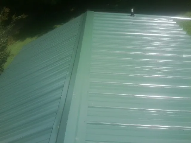 New green metal panels meeting at the ridge of a roof — Flat Roof Repair work by our crew in Shelter Island Heights