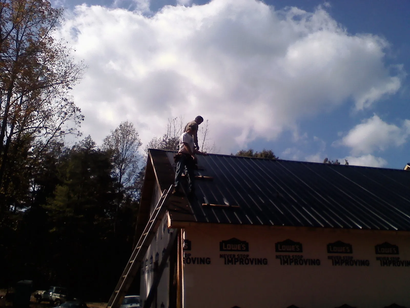 Roofer fastening dark metal panels high against a cloudy sky, from a Roof Inspection job in Shelter Island Heights