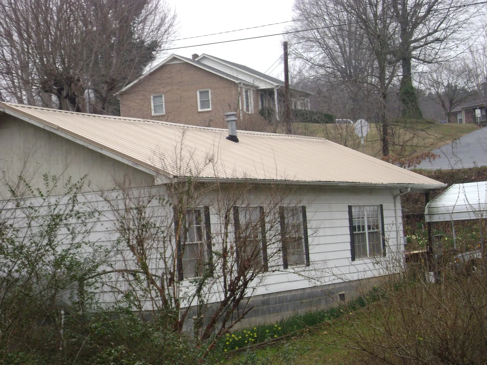 Tan metal roof on a white sided house set into a hillside — Commercial Roofing by Roofing Brothers in Shelter Island Heights